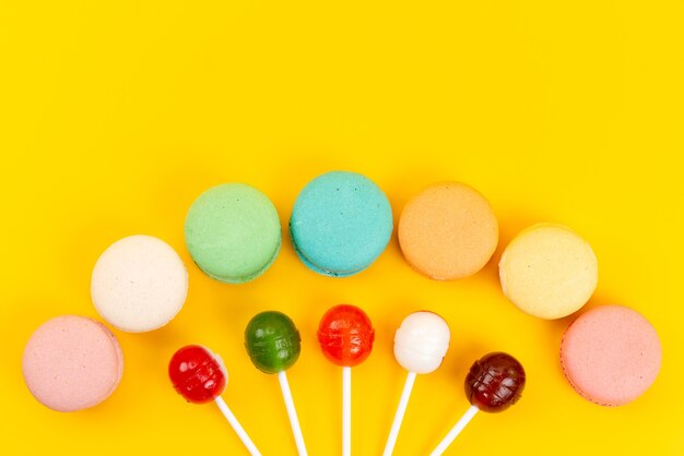 A top view french macarons with sweet and sour lollipops on yellow, cake biscuit bake