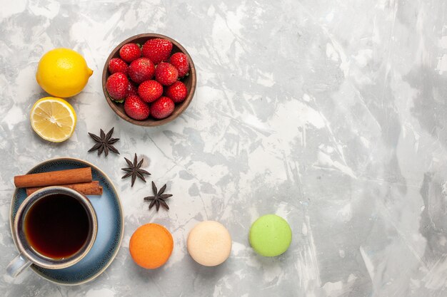 Top view french macarons with tea and fresh strawberries on white surface