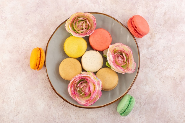 Вид сверху французские макароны вкусные и круглые внутренние тарелки на розовом столе бисквитный торт сладкий сахар