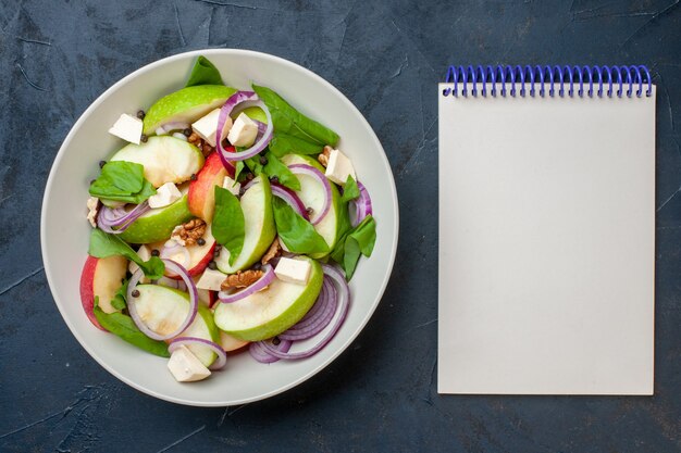 Top view fresh apple salad in bowl notebook on dark blue background