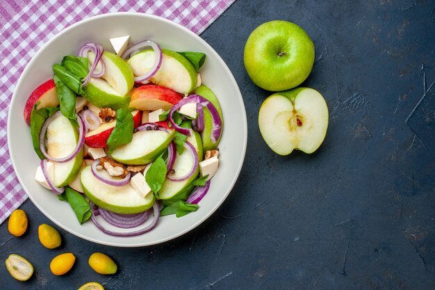 Top view fresh apple salad on round plate apples cumcuat purple and white checkered tablecloth on dark table