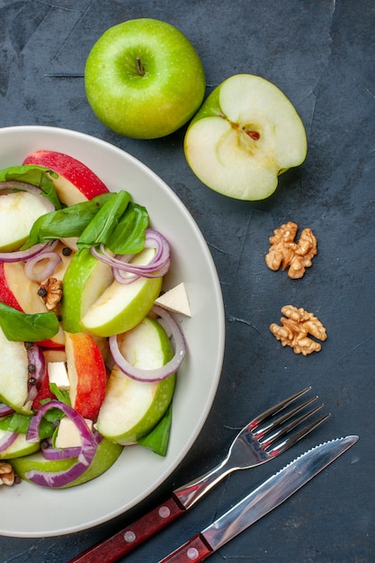 Free photo top view fresh apple salad on round plate apples walnut fork and knife on dark table