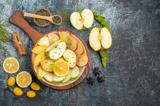 Top view of fresh apple slices on a white plate with lemon and wooden cutting board cinnamon limes on gray background