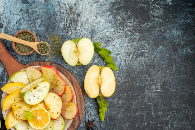 Top view of fresh apple slices on a white plate with lemon on wooden cutting board on gray background