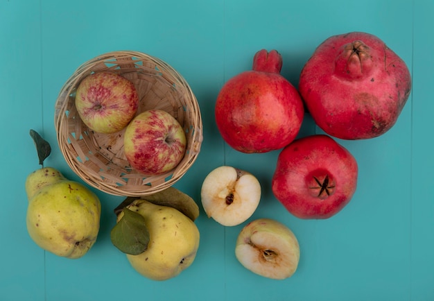 Free photo top view of fresh apples on a bucket with pomegranates and quinces isolated on a blue background