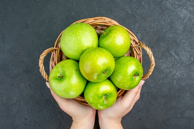 Top view fresh apples in wicker basket in female hand on dark surface