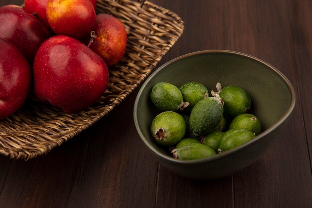 Top view of fresh apples on a wicker tray with feijoas on a bowl on a wooden wall