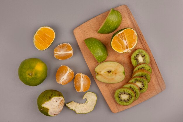 Top view of fresh apples with kiwi slices on a wooden kitchen board with tangerines isolated