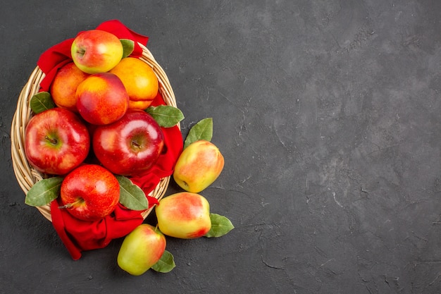 暗いテーブルの果樹のバスケットの中に桃と新鮮な熟した新鮮なリンゴの上面図