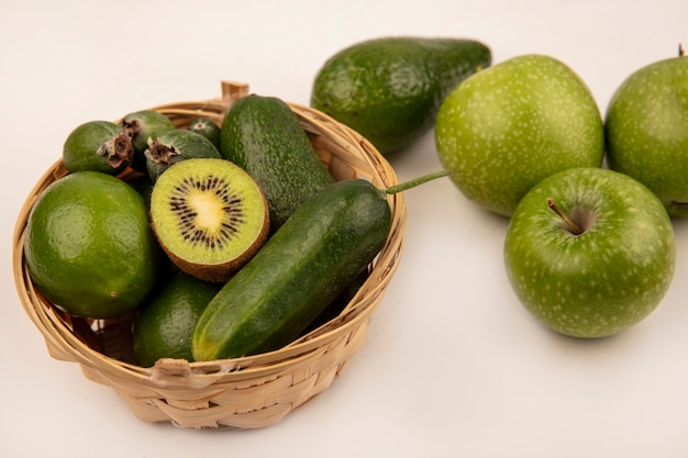 Top view of fresh avocados with cucumber limes and feijoas on a bucket with green apples isolated on a white surface