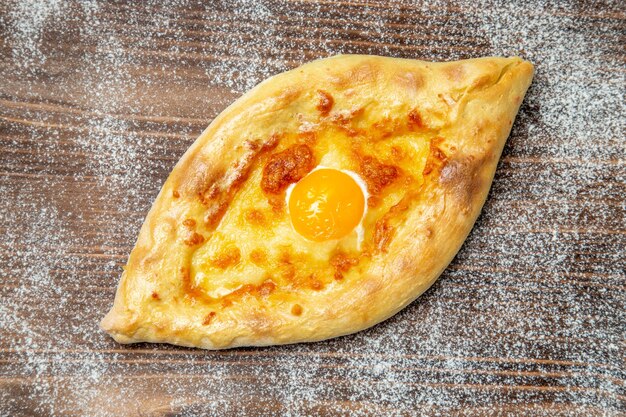 Вид сверху свежеиспеченный хлеб с вареным яйцом на коричневом письменном тесте еда выпечка булочка мука яйцо
