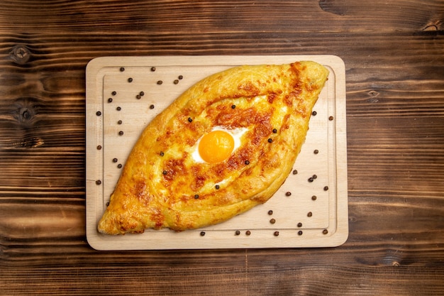 Вид сверху свежеиспеченный хлеб с вареным яйцом на коричневом деревянном столе, тесто, булочка, завтрак, яйца, еда