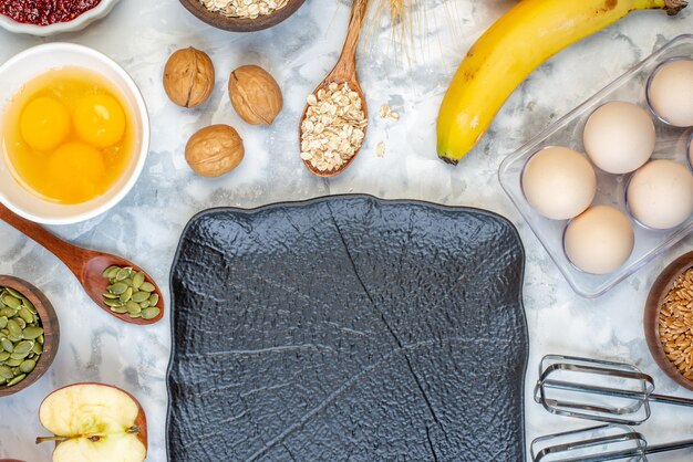 Top view of fresh banana wooden spoon walnuts oats in a brown pot and black tray eggs on ice background