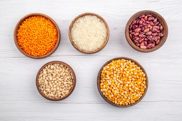 Top view of fresh beans and rice corn kernels yellow lentils in brown bowls on white surface