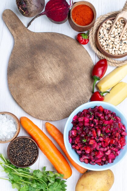 top view of fresh beet salad with sliced vegetables along with raw beans carrots potatoes on white desk, food meal vegetable salad