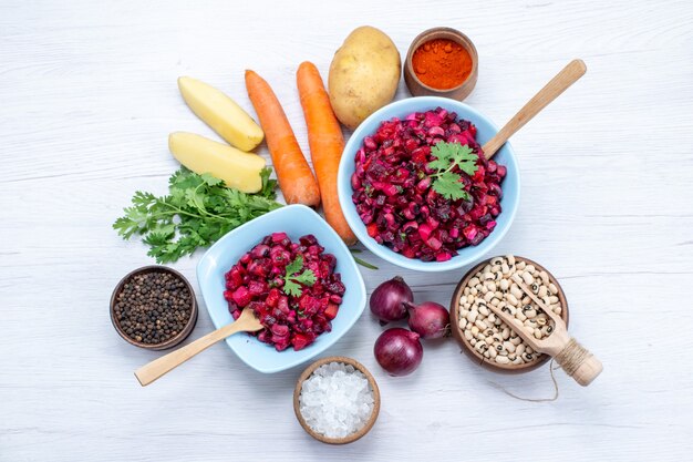 top view of fresh beet salad with sliced vegetables inside blue plates with ingredients on light desk, vegetable salad food meal health snack