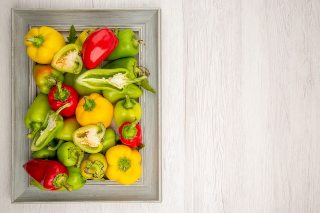 Top view fresh bell-peppers inside frame on white table