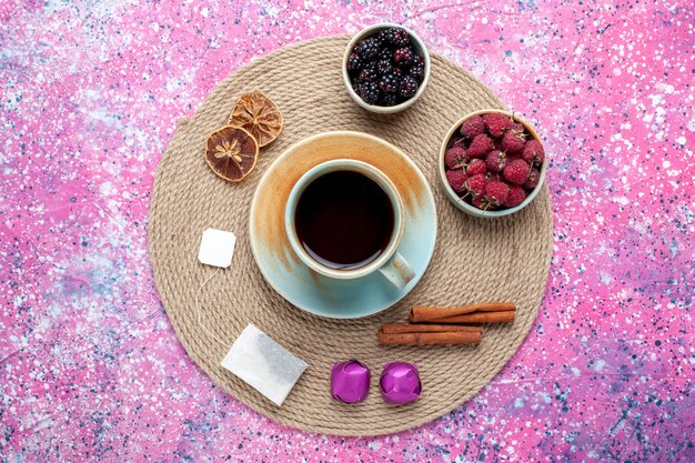 Top view fresh berries raspberries and blackberries with tea and cinnamon on the pink desk.