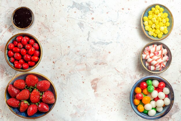 Вид сверху свежие ягоды с конфетами на белом столе, конфеты, ягоды