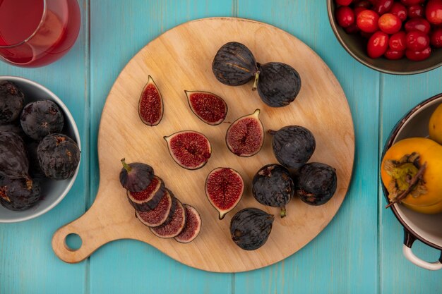 Top view of fresh black mission figs on a wooden kitchen board with persimmon fruits on a bowl on a blue wooden wall