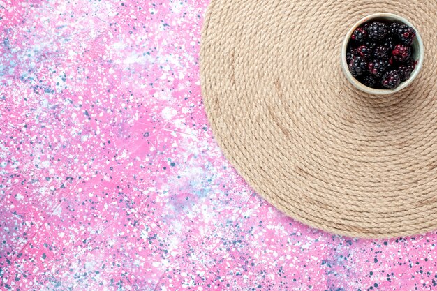 Top view fresh blackberries inside white little pot on pink desk.