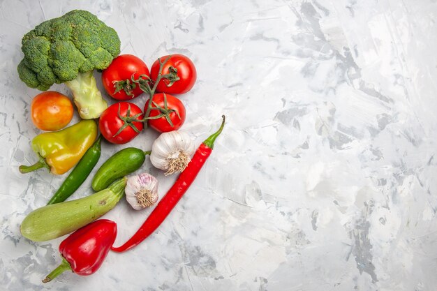 Вид сверху свежей брокколи с овощами на белом столе, салате, спелой здоровой диете