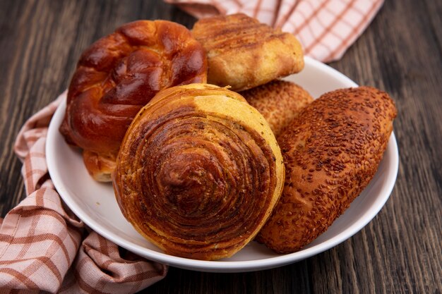 Top view of fresh buns such as patties gogals on a plate on a checked cloth on a wooden background with copy space