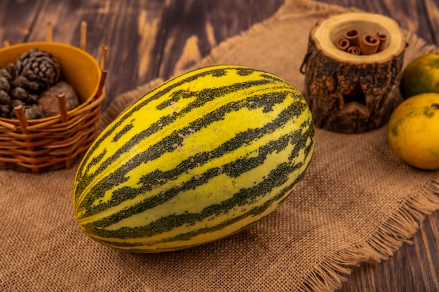 Top view of fresh cantaloupe melon on a sack cloth with cinnamon sticks with pine cones on a bucket on a wooden wall