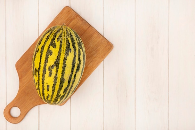 Free photo top view of fresh cantaloupe melon on a wooden kitchen board on a white wooden surface with copy space