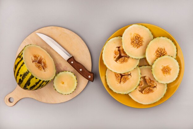 Top view of fresh cantaloupe melon on a wooden kitchen board with knife with melon slices on a yellow plate on a white wall