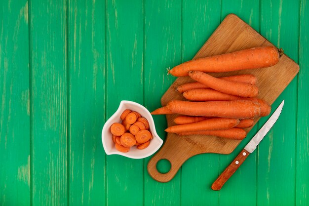 Top view of fresh carrots on a wooden kitchen board with knife on a green wooden wall with copy space