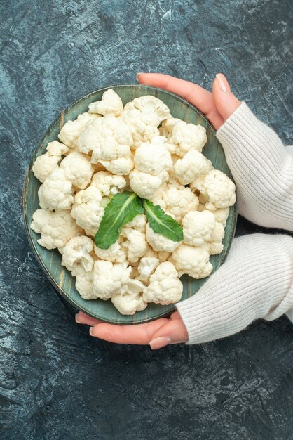 Top view fresh cauliflower inside plate in female hands on light-grey table