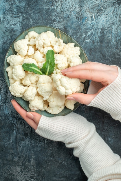 Top view fresh cauliflower inside plate in female hands on light-grey table