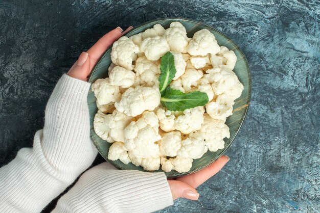 Top view fresh cauliflower inside plate in female hands on light-grey table