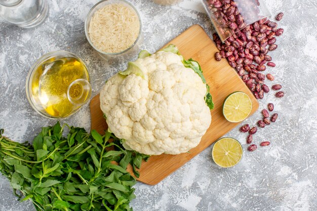 Top view of fresh cauliflower with oil greens and beans on grey surface