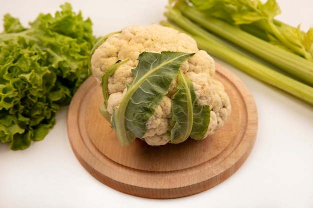 Top view of fresh cauliflower on a wooden kitchen board with lettuce and celery isolated on a white wall