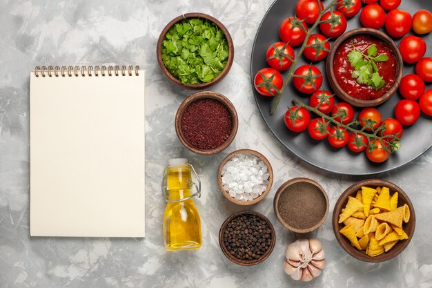 Top view fresh cherry tomatoes inside plate with different seasonings and oil on white surface