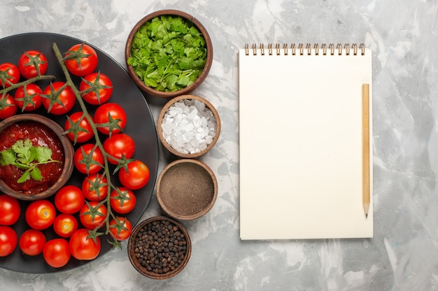 Free photo top view fresh cherry tomatoes inside plate with different seasonings on the white surface