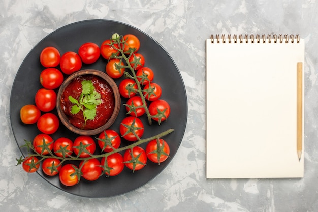 Top view fresh cherry tomatoes inside plate with notepad on the white surface