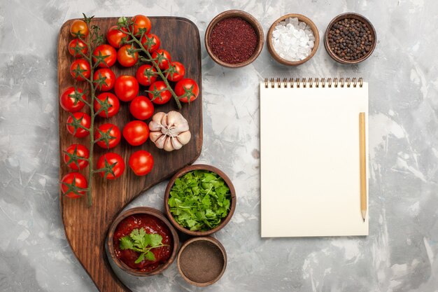 Top view fresh cherry tomatoes with seasonings notepad and greens on white surface