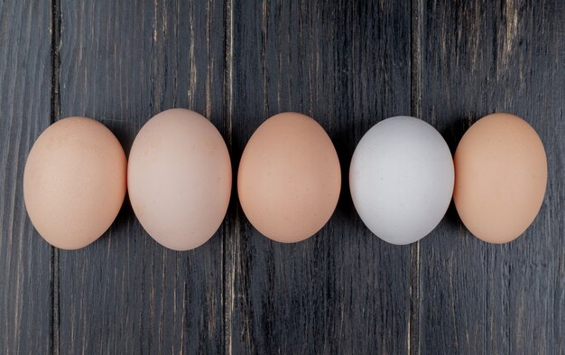 Top view of fresh chicken eggs arranged in a line on a wooden background