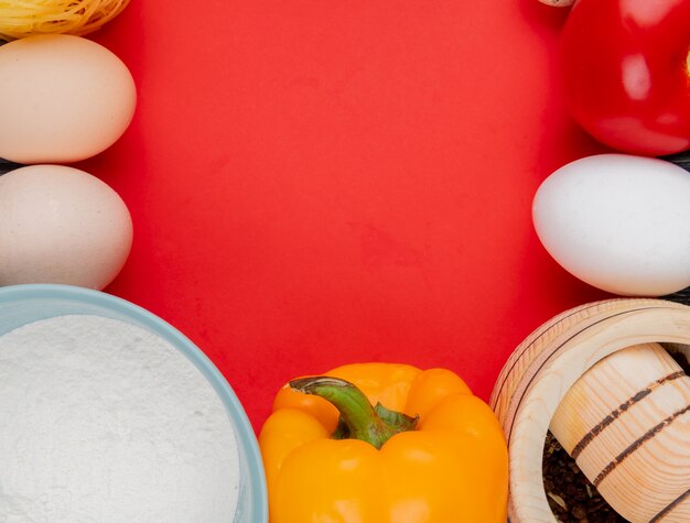 コピースペースと赤の背景に青いボウルに小麦粉と新鮮な鶏の卵のトップビュー