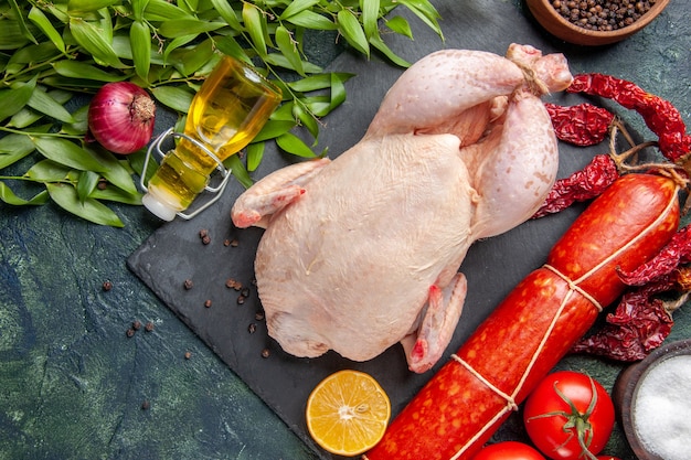 Вид сверху свежего цыпленка с красными помидорами и колбасой на темной поверхности
