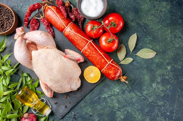 Вид сверху свежего цыпленка с красными помидорами и колбасой на темной поверхности