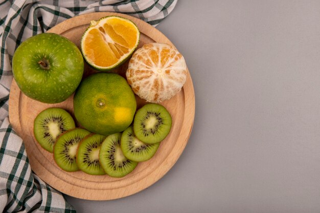 Vista dall'alto di fette di kiwi tritate fresche su una tavola di cucina in legno su un panno controllato con mela verde e mandarino con spazio di copia