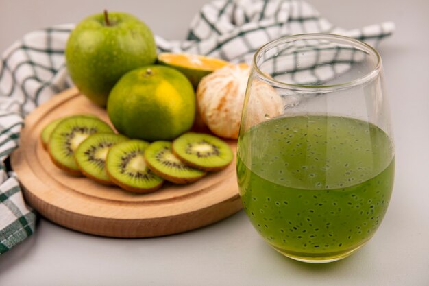 Top view of fresh chopped kiwi slices on a wooden kitchen board on a checked cloth with green apple and tangerine with fresh kiwi juice on a glass bottle