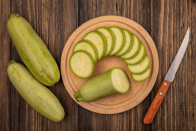 Foto gratuita vista dall'alto di zucchine fresche tritate su una tavola da cucina in legno con coltello con zucchine isolato su una superficie di legno