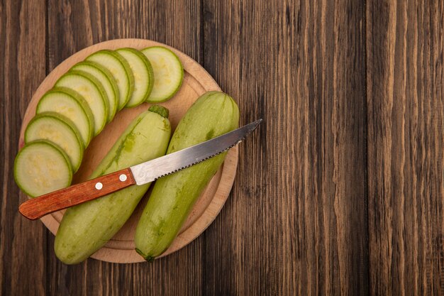 Top view of fresh chopped zucchinis on a wooden kitchen board with knife on a wooden wall with copy space