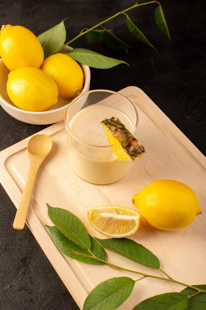 A top view fresh cocktail yummy cooling drink inside little glass near wooden cream desk along with yellow lemons on the dark