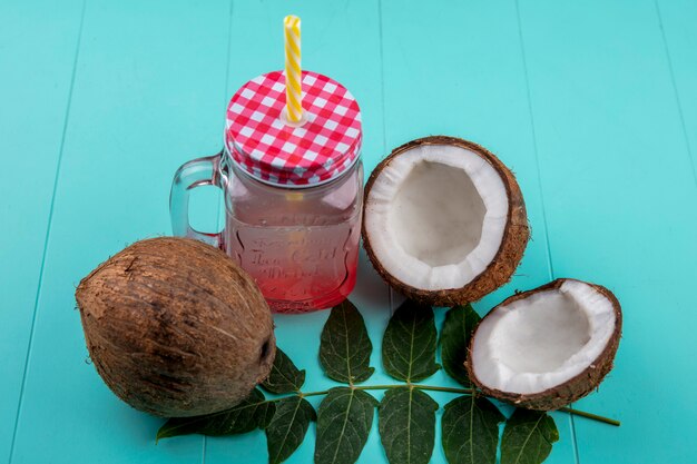 Top view of fresh coconut with leaves and juice in glass jar on blue